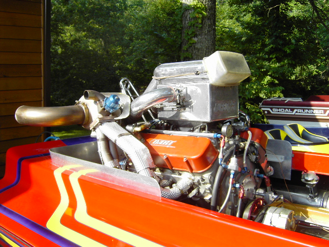 Supercharged V8 with orange valve covers and chrome exhaust in a red race boat