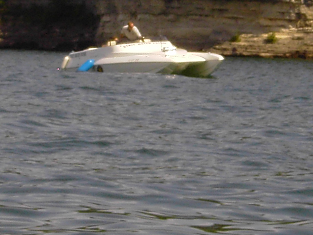 White performance powerboat sitting on calm water with a person aboard near a rock bluff