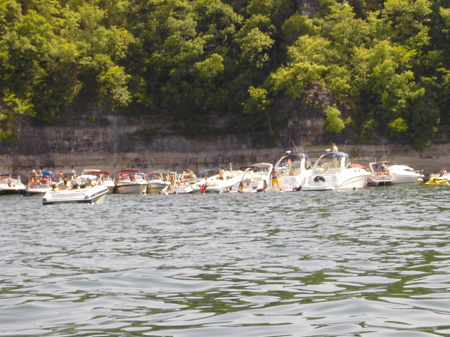 Several boats docked near a cliff with trees; Supermotors.net logo visible