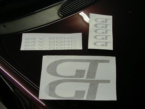 1994 Ford Probe - Decals for a vehicle, including 'GT' and '24V DOHC' text, are laid out on a dark car's hood.
