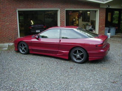 1994 Ford Probe - A red 1994 Ford Probe is parked outside a brick garage, with another vehicle visible inside.
