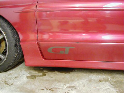 1994 Ford Probe - Close-up of a red car's side panel, showing a GT badge and part of the front wheel.