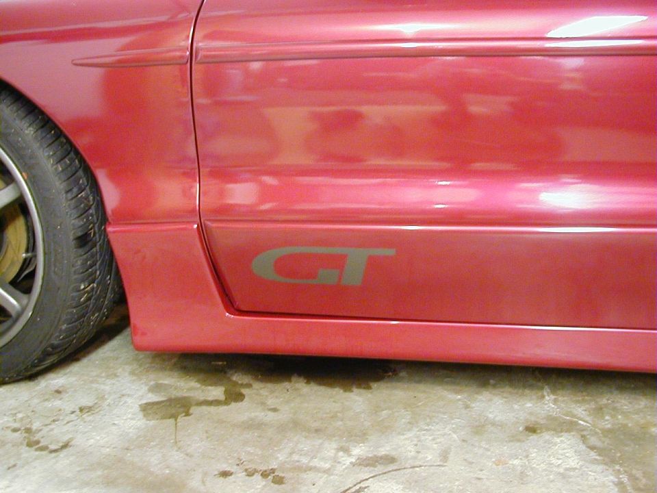 Red car side panel with a grey GT badge and a portion of the front tire visible