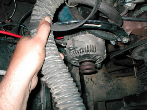 1979 Ford Bronco - A close-up view of engine components, including an alternator and hoses, with a hand interacting with the assembly.