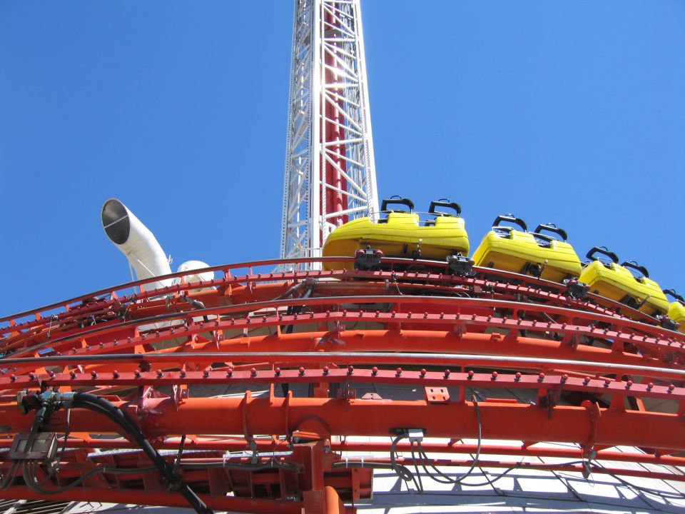 Red roller coaster track with yellow cars and white tower against blue sky
