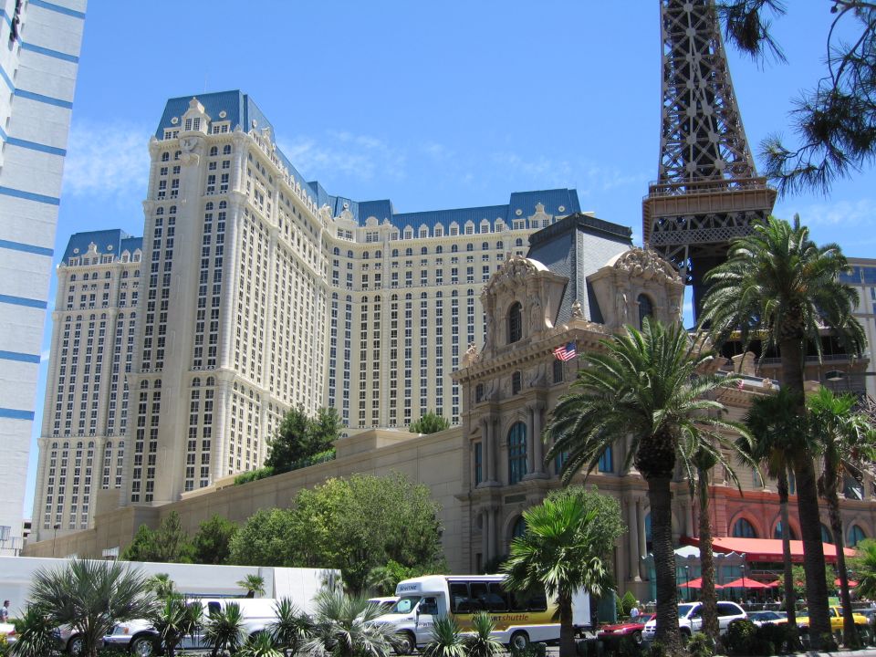 White limousine, bus, and SUV parked in front of a large hotel with a Paris Eiffel Tower replica