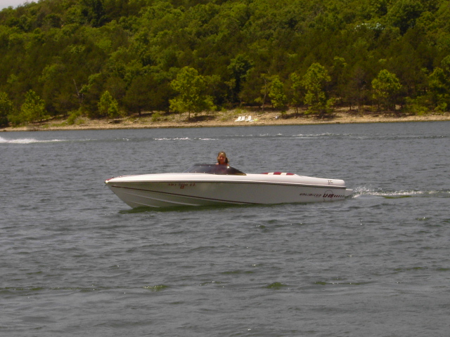 White open-bow sport boat on a lake with one person at the helm