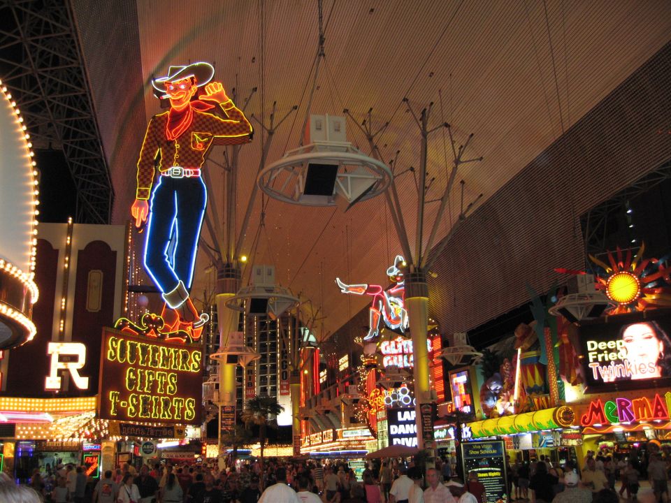 Neon cowboy sign and other bright signs over a crowded street at night