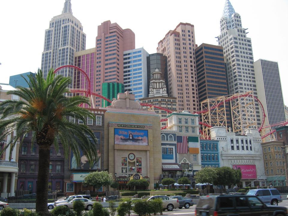 New York-New York Hotel and Casino with roller coaster and palm tree. Several cars are parked in front