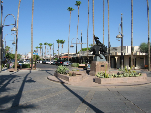 Street scene with a statue of a cowboy on a bull, palm trees, and parked cars