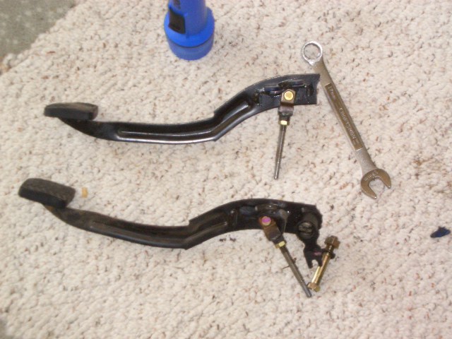 Two black pedal assemblies with pushrods on carpet next to a combination wrench