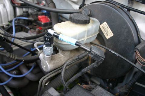 1994 Ford Bronco - Close-up of a cruise control pressure switch and inline fuse assembly attached to the brake master cylinder.