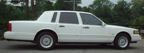 1997 Ford Crown Victoria - Side profile of a white sedan with tinted windows and wire-spoke wheels.