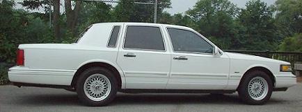 1997 Ford Crown Victoria - A white Lincoln Town Car is shown from the side, parked near trees and a wooden railing.