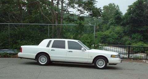 1997 Ford Crown Victoria - A white 1997 Ford Crown Victoria sedan is seen from the side, parked outdoors with trees and a fence in the background.