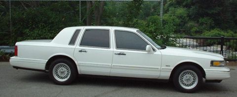 1997 Ford Crown Victoria - This white Lincoln Town Car is shown from the side. The vehicle has tinted windows and a distinctive body style.