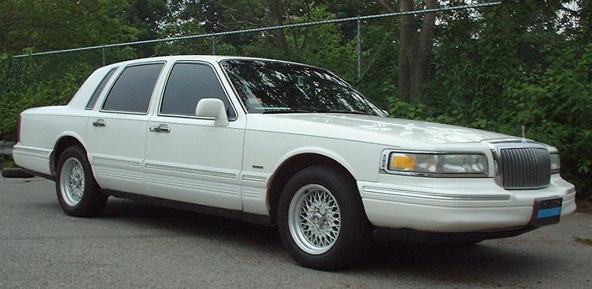 White sedan with chrome grille and wire wheels, parked on asphalt