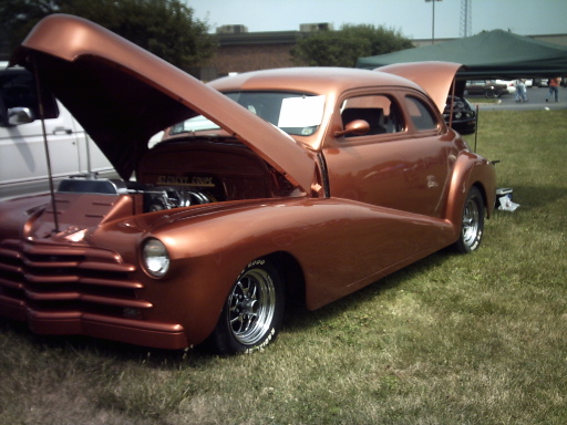 Copper customized coupe with hood open, showing engine. Chrome wheels and wide tires visible