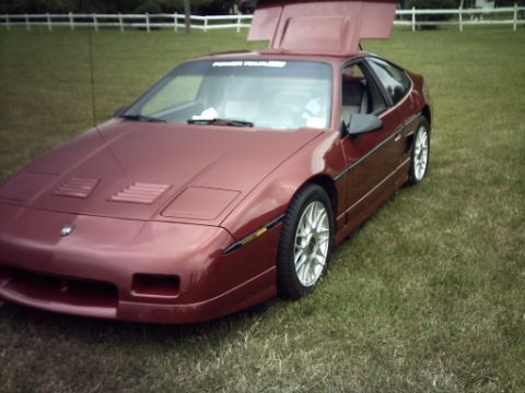 1995 Ford Probe - A red Pontiac Fiero is parked on a grassy field with its doors raised.