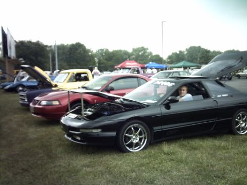 1995 Ford Probe - A line of cars are parked on grass at an outdoor event, with one black Ford Probe in the foreground.