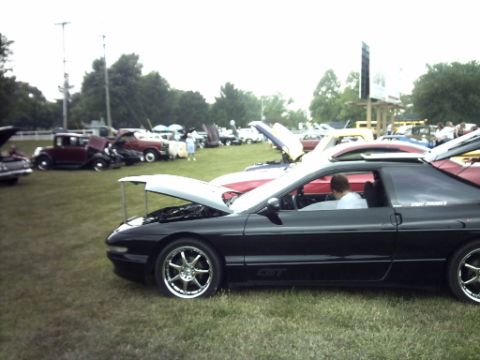 1995 Ford Probe - A black 1995 Ford Probe is displayed with its hood open at a car show, alongside other vehicles.