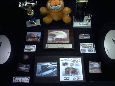 1995 Ford Probe - A collection of car show awards and photos, including a Garfield plush toy and trophies, displayed on a dark surface.