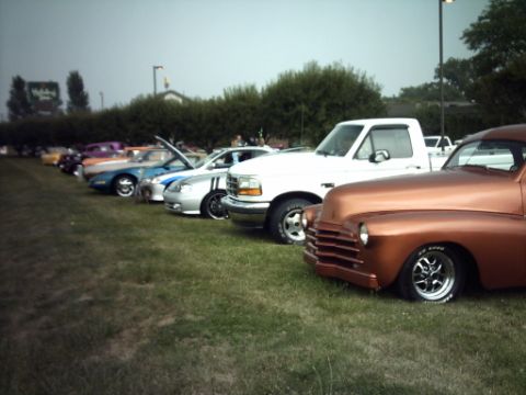 1995 Ford Probe - A row of vehicles, including a copper-colored classic car and a white pickup, are parked on grass at an outdoor event.