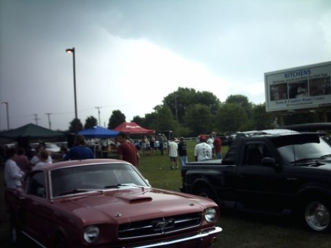 1995 Ford Probe - A red classic car and a black pickup truck are parked at an outdoor car show with tents and people.
