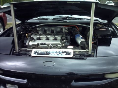 1995 Ford Probe - The engine bay of a black car is visible with the hood propped open. Text on the lower right reads SUPERMOTORS.