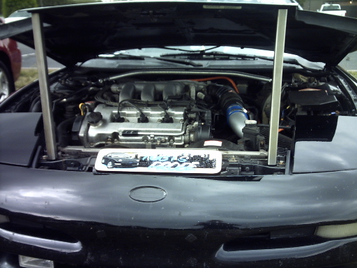 Black car engine bay with hood open. Visible text: SUPERMOTORS