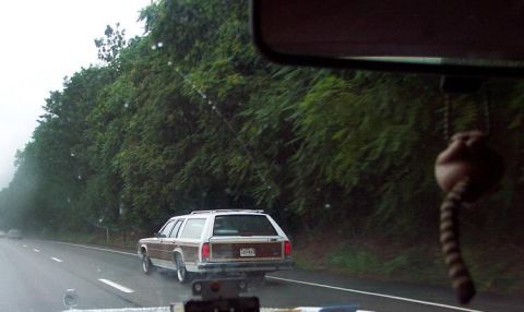 1985 Ford LTD Crown Victoria - A wood-paneled station wagon travels down a highway on a rainy day.