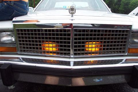 1985 Ford LTD Crown Victoria - The front of a white Ford Crown Victoria is shown, with a person sitting on the hood.