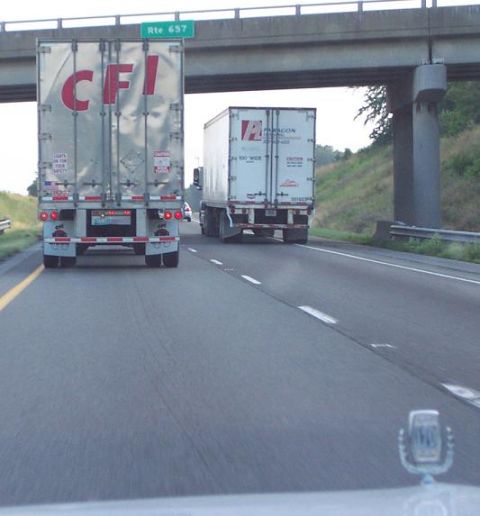 1985 Ford LTD Crown Victoria - Two semi-trucks travel down a highway under an overpass, with a sign indicating Rte 657.