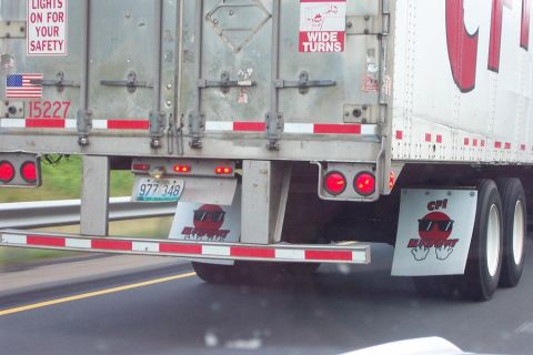 1985 Ford LTD Crown Victoria - Semi-trailer truck's rear end shows safety stickers, license plate, and custom mudflaps.