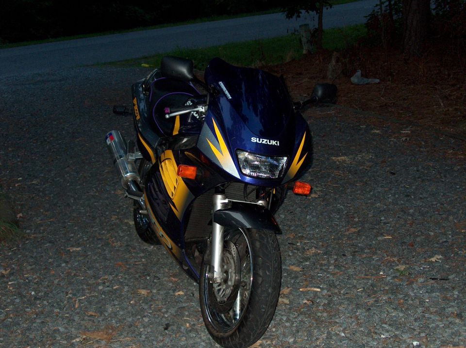 Blue and yellow Suzuki sportbike parked on gravel at dusk, front three-quarter view