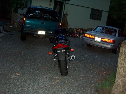2002 Suzuki TL1000R - A dark-colored motorcycle is parked in a gravel driveway with a teal SUV and a silver sedan nearby.