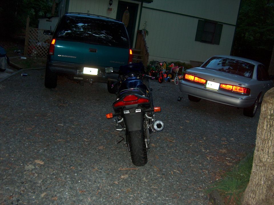 Motorcycle parked in driveway next to a teal SUV and a silver sedan