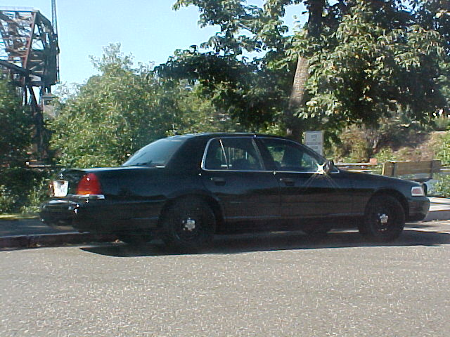 Black sedan parked on street, trees and bridge in background