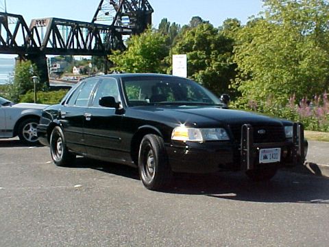 1999 Ford Crown Victoria - A black Ford Crown Victoria police car is parked outdoors with a bridge in the background.