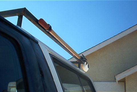 1986 Ford Bronco - A shovel is secured to the roof rack of a vehicle, with a house visible in the background.