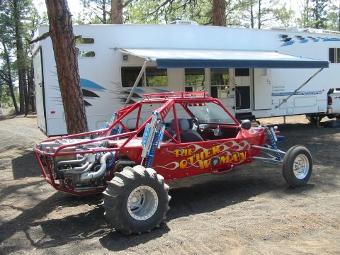 1993 Ford Taurus - Rear three-quarter view of a red tube-chassis sand rail lettered "THE OTHER WOMAN" in yellow flame graphics, with blue King coil-over shock…