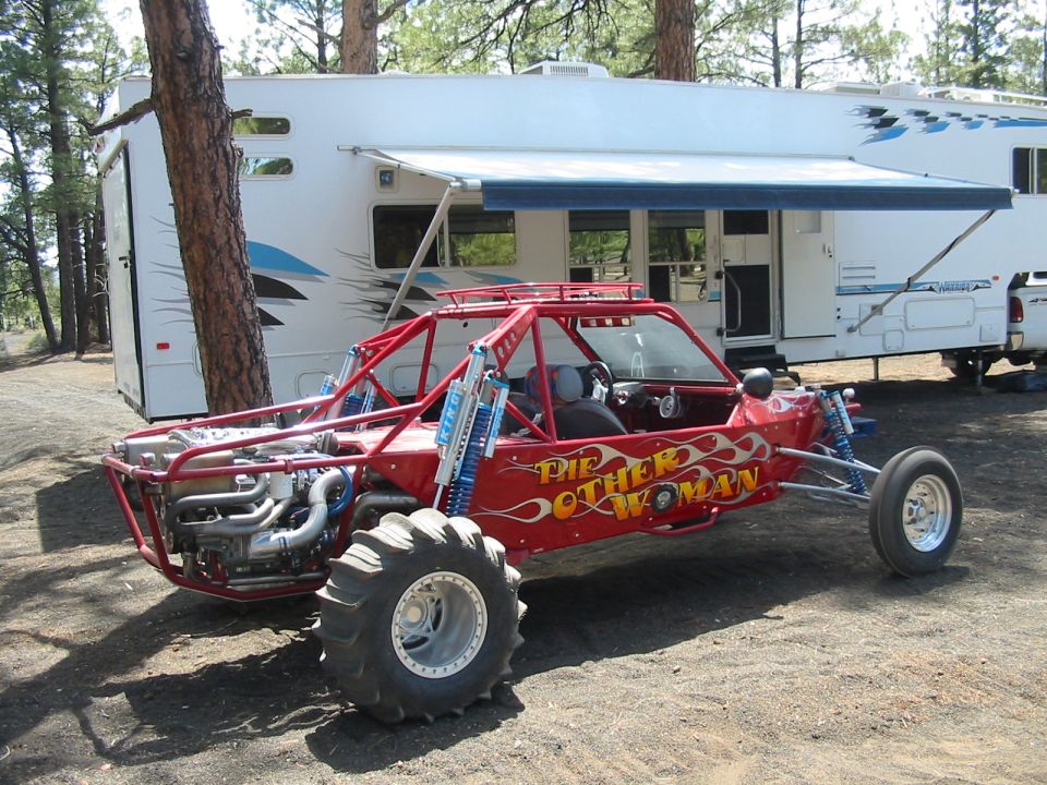 Red sand rail lettered The Other Woman with blue King shocks and paddle tires at a pine campsite