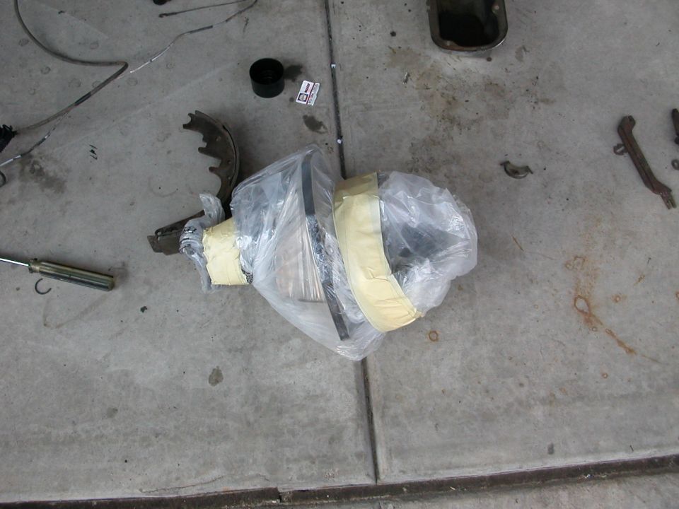 Axle shaft and hub wrapped in plastic and tape on a garage floor beside a brake shoe