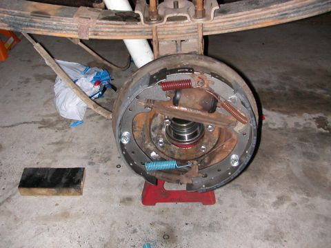 1984 Ford Bronco - The rear drum brake assembly is shown with new brake shoes and springs, supported by a red jack stand.