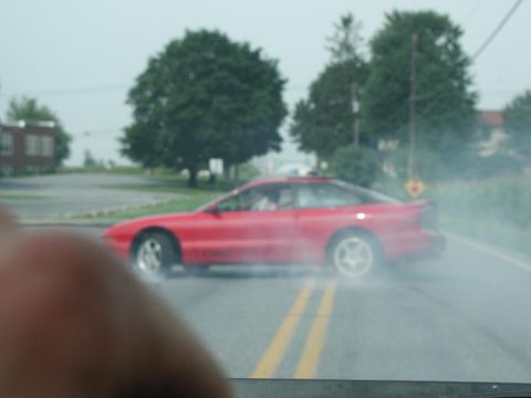 1997 Ford Probe - A red coupe drifts on a road, creating smoke from its tires.