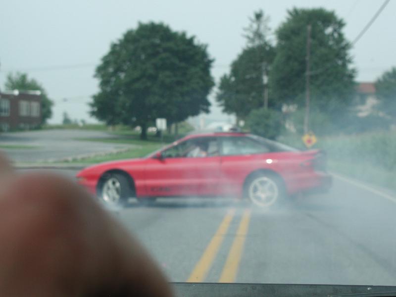 Red coupe with smoke coming from tires, seen from the side