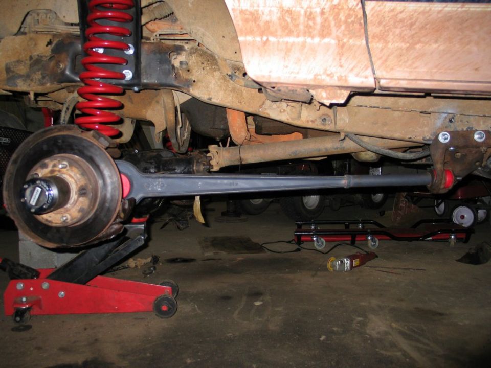 Underside of lifted truck showing gray radius arm, red coil spring, and axle hub on a floor jack