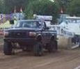 1994 Ford F-150 - A modified pickup truck competes in a truck pull event, kicking up dirt as it goes.