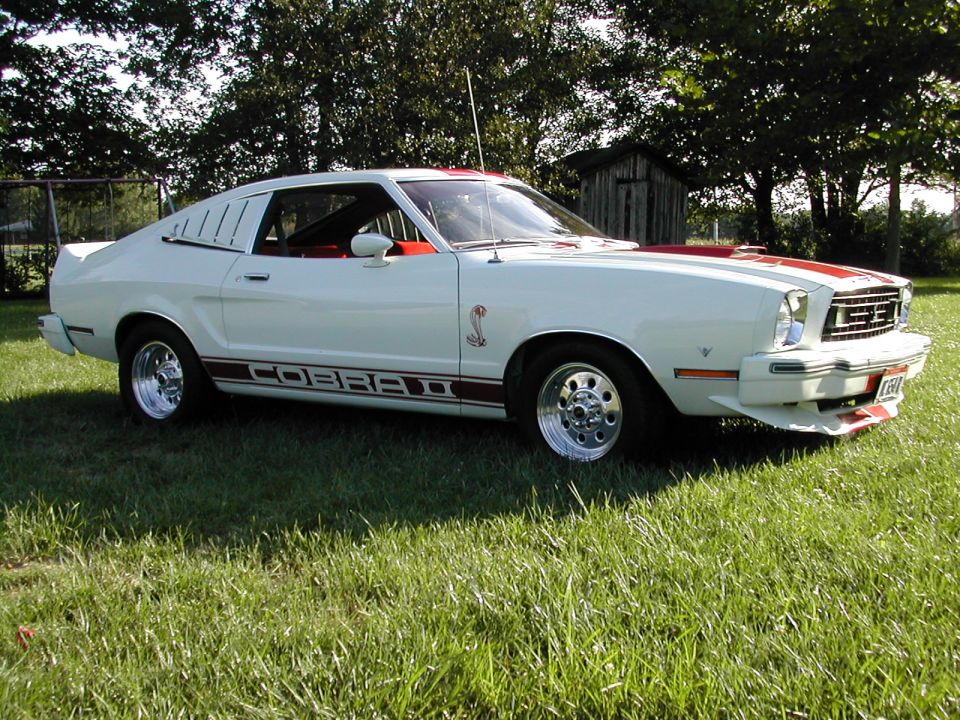 White 1978 Ford Mustang II Cobra II with red stripes and side decals, parked on grass