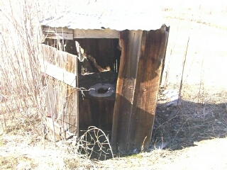 1986 Ford Bronco - An old, weathered outhouse stands in a dry, grassy field, showing signs of significant disrepair.